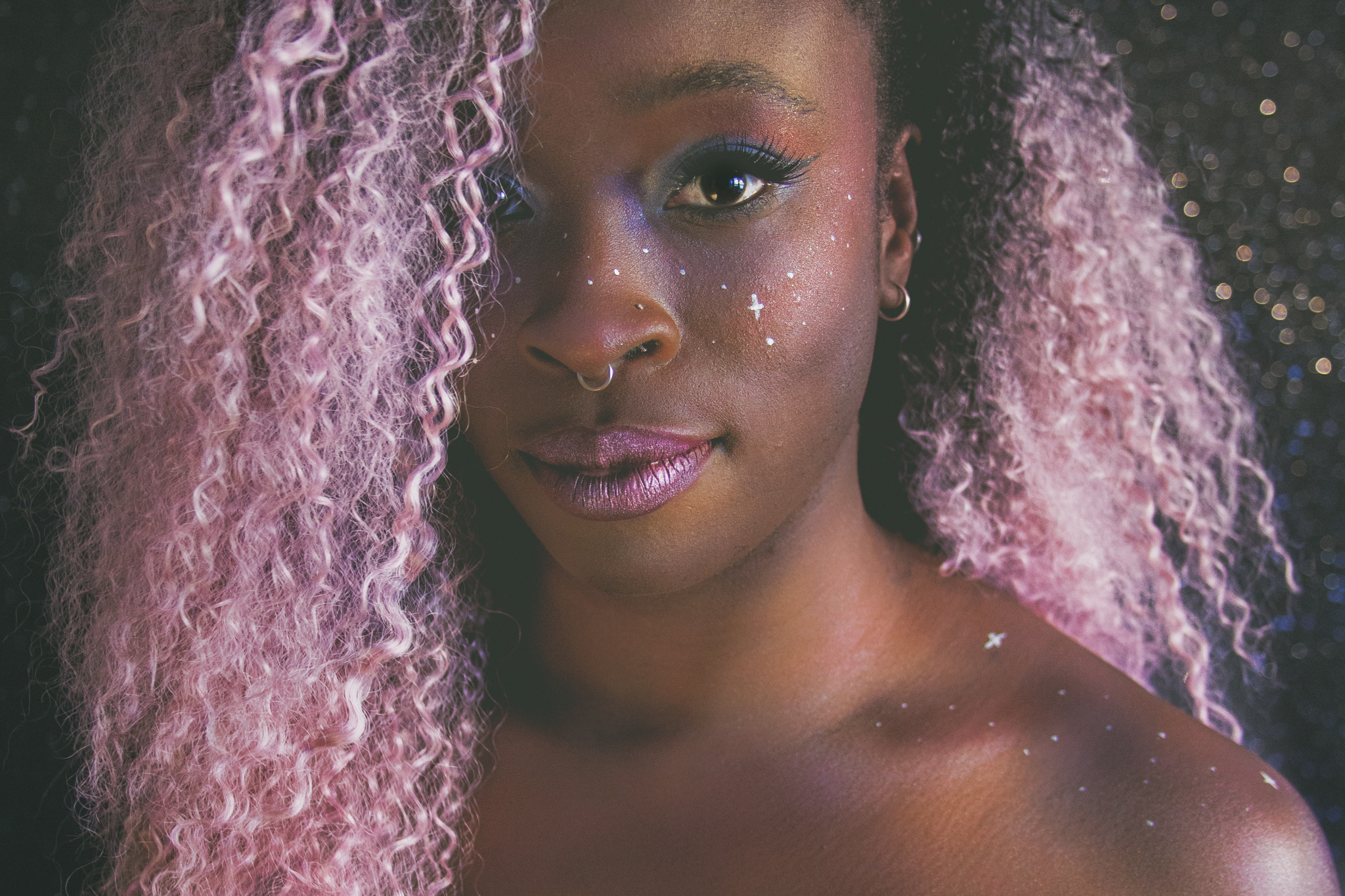 close up of Danielle Boachie's face, they are wearing purple lipstick and have curly, long purple hair, looking directly into the camera.